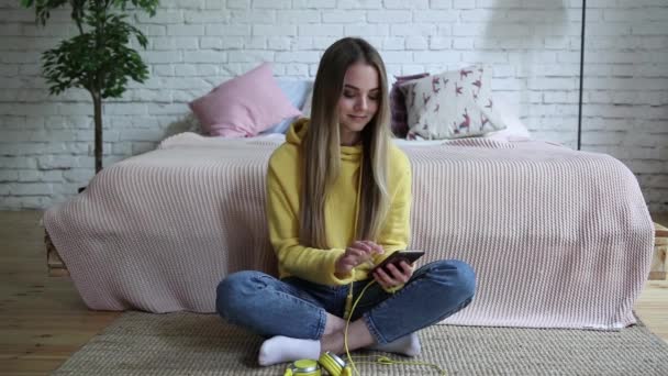 Девушка слушает музыку с наушниками из телефона дома . — стоковое видео