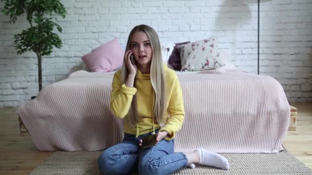 Piękna młoda kobieta w domu siedzi na podłodze i rozmawia przez telefon. — Wideo stockowe