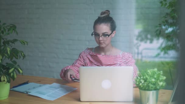 Genomtänkta koncept. Kvinna som arbetar på en dator på ett kafé medan du blickar genom fönsterglas. — Stockvideo