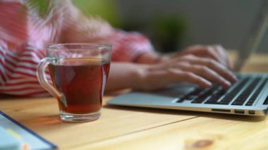 bir kız masadan, şeffaf bir kupa çay çalışırken, çay içiyor.