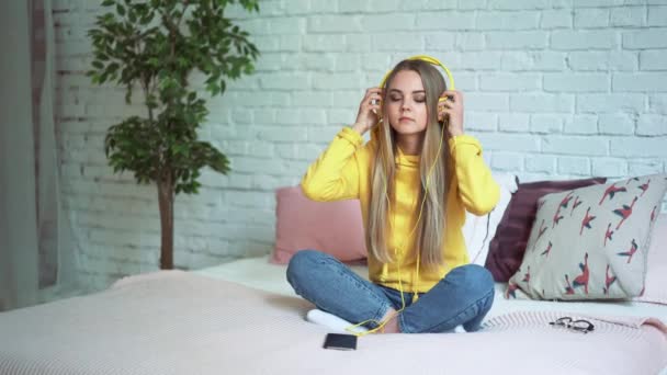 Hermosa chica escuchando música en los auriculares en la cama y relajante usando el teléfono — Vídeos de Stock