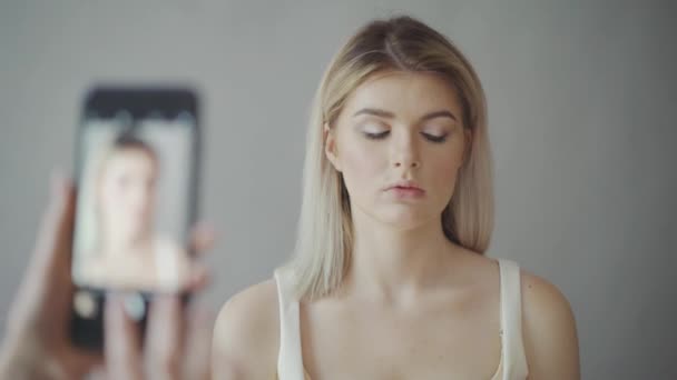 메이크업 아티스트는 휴대 전화에는 모델의 사진을 걸립니다. 어두운 입술, 회색 배경입니다. 메이크업 — 비디오