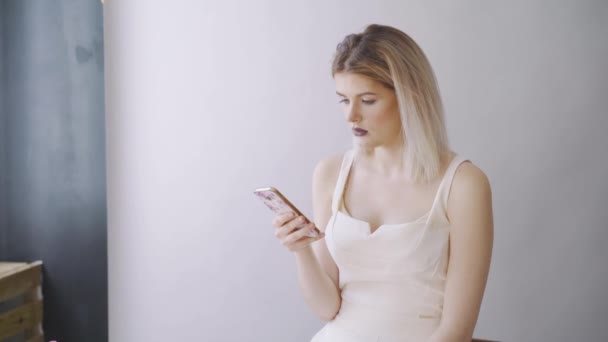 Cool meisje is kijken naar foto's op smartphone, ze wordt verplaatst, communicatie concept, grijze achtergrond — Stockvideo