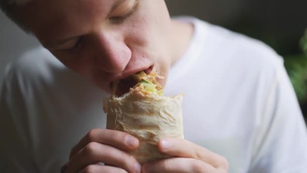 Joven, estudiante sentado en casa comiendo comida rápida. Shawarma, Shawarma, Shawarma. Alimentos frescos saludables o poco saludables . — Vídeos de Stock