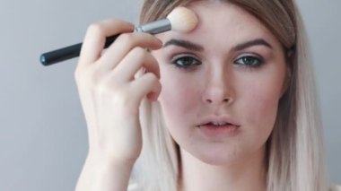 Kalıcı makyaj. Genç güzel kız makyaj fırça ile yanaklarda yapma.