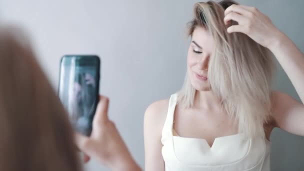 Maquillaje artista toma fotos de la modelo en el teléfono. Labios oscuros, fondo gris. Maquillaje — Vídeos de Stock