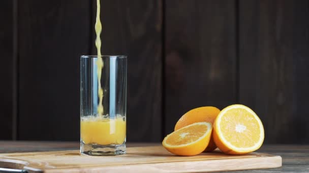 Freshly squeezed orange juice in a glass. Pour, squeeze orange juice. On a wooden background. — Stock Video