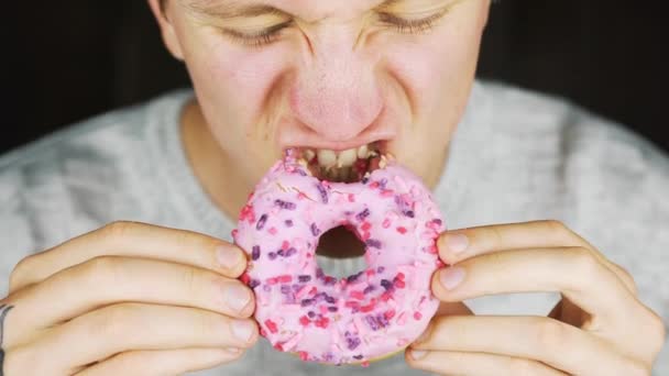Portret van een jonge hongerige man het eten van een donut — Stockvideo