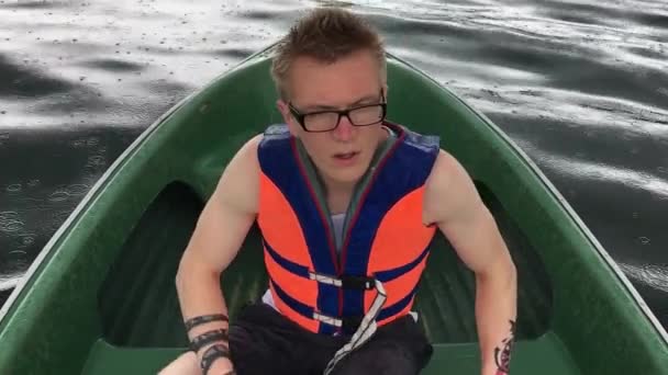 Een jonge man in een boot roeien houten roeiriemen op het water. Zwemvest op het lichaam van een man. — Stockvideo