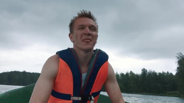 A young man in a boat rowing wooden oars on the water. Life jacket on the body of a man. — Stock Video