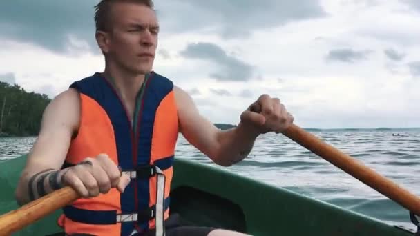 Un giovane su una barca a remi di legno sull'acqua. Giubbotto di salvataggio sul corpo di un uomo . — Video Stock