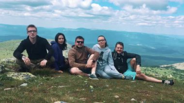 Bir grup arkadaşıyla birlikte, dağın tepesinde oturan turist