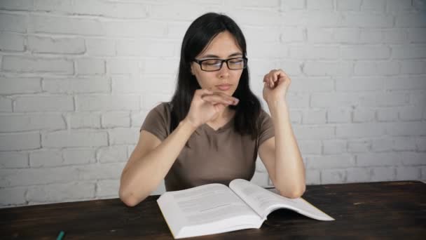 Flickan sitter vid ett vitt bord med glasögon som en bok, dagbok. Dålig syn. — Stockvideo