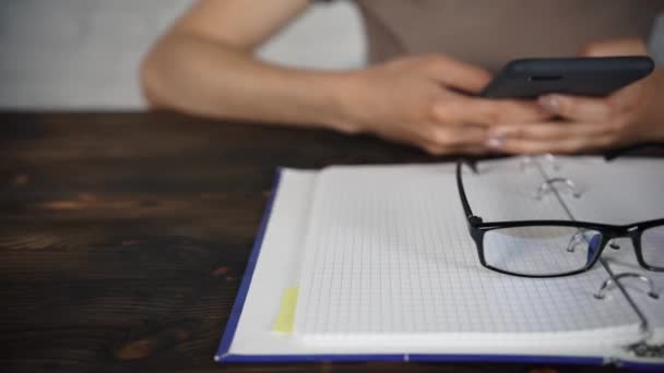 Flickan sitter vid ett vitt bord med glasögon som en bok, dagbok. Dålig syn. — Stockvideo