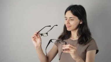 Genç kadın yeni gözlüklerini gri arka planı yansıtmadaki içinde kontrol. Gri arka plan üzerinde gözlüklü genç kadın. Gözlük ile güzel kız.