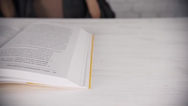 Dívka sedí u bílého stolu s brýlemi čte knihu, diář. Špatný zrak. — Stock video