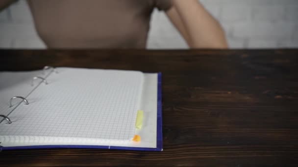 Девушка сидит за белым столом в очках, читает книгу, дневник. Плохое зрение . — стоковое видео