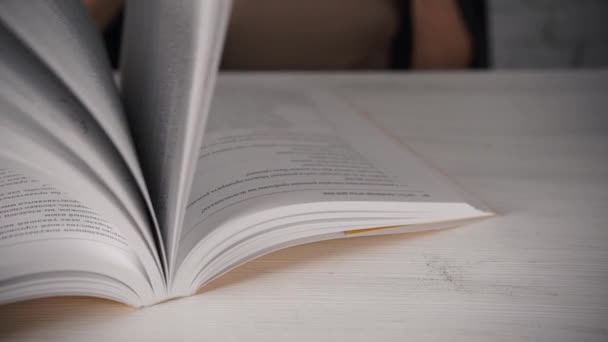 Chica sentada en una mesa blanca con gafas leyendo un libro, diario. Mala vista. . — Vídeo de stock