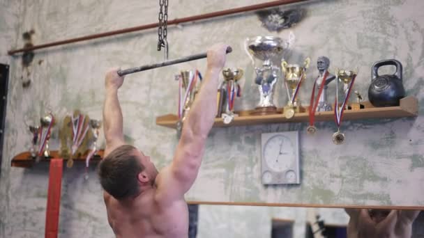 Tilt up of shirtless sportsman doing pull-ups on bars during cross-training workout at gym — Stock Video