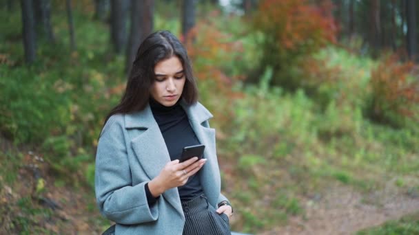 Glückliche junge Frau schickt SMS, SMS im Park — Stockvideo