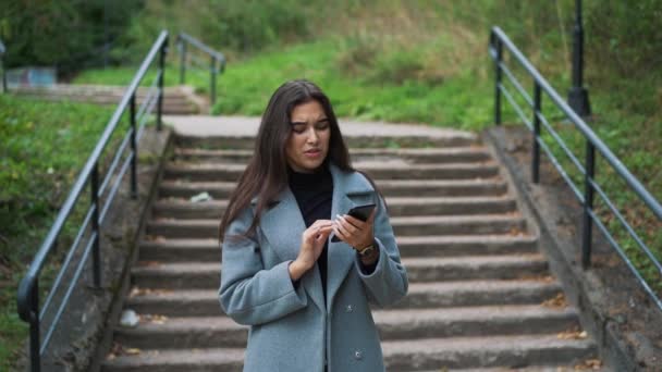 Glad ung kvinna skicka sms, skicka SMS i parken — Stockvideo