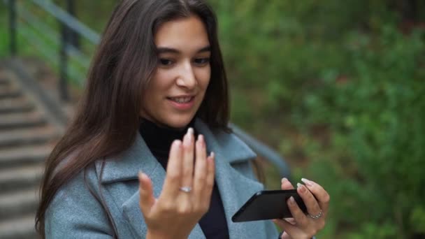 Счастливая молодая женщина отправляет смс, смс в парке — стоковое видео