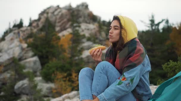 Дівчина їсть хот-дог на вершині гори . — стокове відео
