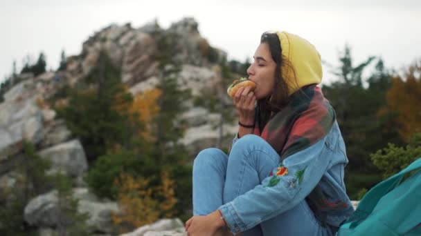 Flicka äter varmkorv på toppen av berget. — Stockvideo