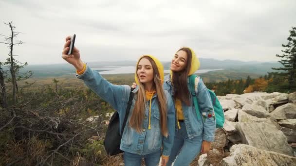 Duas jovens mulheres felizes dançando e levantando os braços no belo topo da montanha sobre o céu do pôr do sol . — Vídeo de Stock