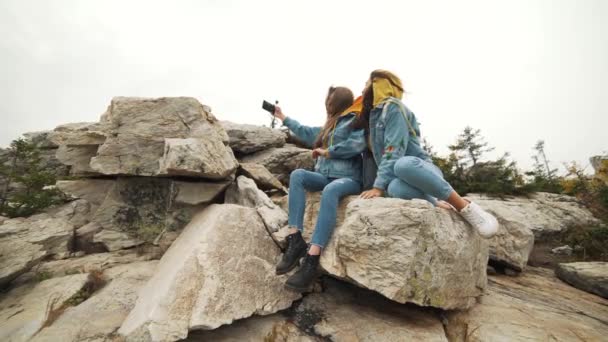 Две молодые счастливые женщины танцуют и поднимают руки на красивой вершине горы над закатом . — стоковое видео