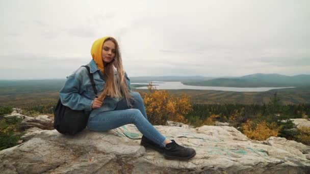 Una joven sentada en la cima de la montaña mirando un hermoso paisaje pensando en la vida. Una chica de vacaciones . — Vídeos de Stock