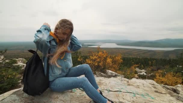 Una joven sentada en la cima de la montaña mirando un hermoso paisaje pensando en la vida. Una chica de vacaciones . — Vídeos de Stock