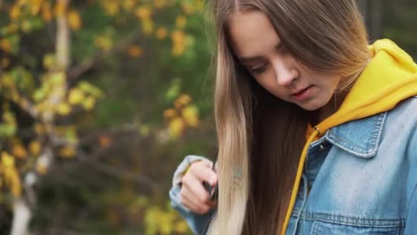 Κορίτσι όμορφο φοιτητής, χαμογελώντας, χτένες μακριά μαλλιά στο πάρκο. Ανάπαυση κατά τη διάρκεια μελέτης — Αρχείο Βίντεο