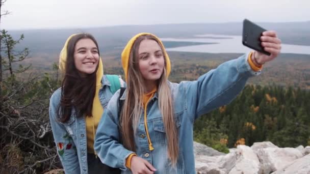 Dua wanita muda yang bahagia menari dan mengangkat tangan di puncak gunung yang indah di langit matahari terbenam . — Stok Video
