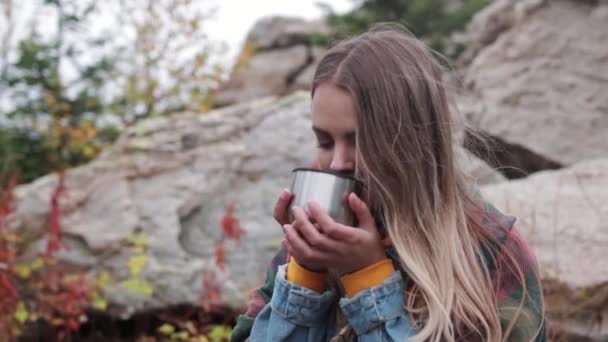 Turista beber té de una taza de un termo contra las montañas — Vídeo de stock