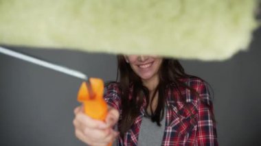 Casual genç güzel kadın giyim gülümseyen holding boya rulo duvar resmi gri arka plan üzerinde izole için. Araçlar, aksesuarlar, daire oda onarmak için araçlar. Ev onarım