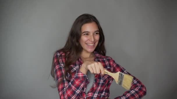 Una mujer vestida de día, bailando y cantando, sosteniendo un cepillo para reparar, herramientas para reparar habitaciones de apartamentos, aislada sobre un fondo gris. Reparación casera — Vídeo de stock