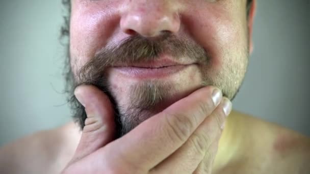 Schoonheid, verzorging en mensen concept - jonge man op zoek naar de spiegel en de baard scheren met snoeischaar of elektrisch scheerapparaat thuis badkamer — Stockvideo