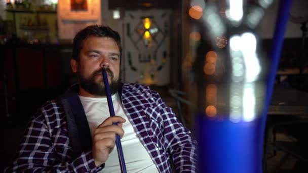 Молодой человек курит кальян в баре . — стоковое видео