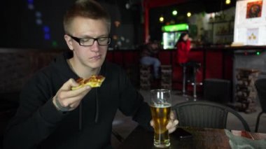 Adam pizza yiyor. O bir parça pizza elinde tutar ve bir iştahla yiyor.