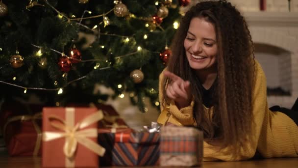 Vrouw opent een nieuw jaar geschenk onder de kerstboom — Stockvideo