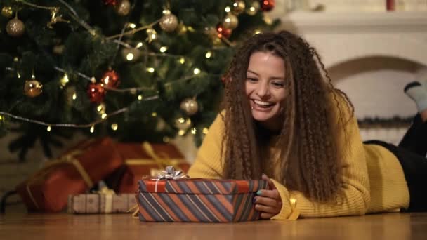 Vrouw opent een nieuw jaar geschenk onder de kerstboom — Stockvideo