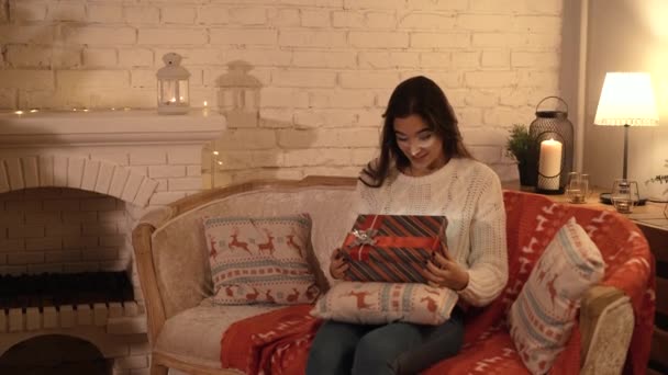 A menina faz um desejo e abre um pacote de presente de Natal. o conceito de férias e Ano Novo. a menina está feliz e sorrindo com um presente de Natal em suas mãos . — Vídeo de Stock