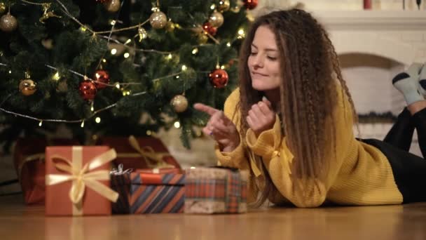 Vrouw opent een nieuw jaar geschenk onder de kerstboom — Stockvideo