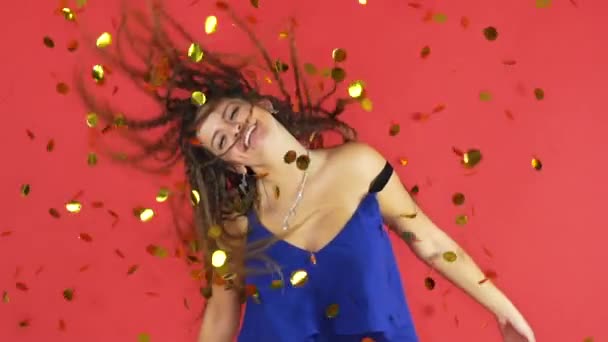 Женщина празднует Новый год на красном фоне с золотыми конфетти — стоковое видео