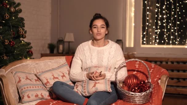 Blogger κορίτσι που κάθεται στο σπίτι στον καναπέ, μιλά για την Πρωτοχρονιά και τα Χριστούγεννα. — Αρχείο Βίντεο