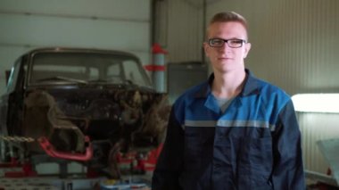 Bir genç güzel araba tamircisi araba atölye, kırık bir araba arka plan olarak portresi. Konsept: makine tamir, tanılamada, uzman onarım, bakım.