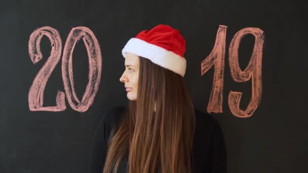 サンタ帽子 黒いスレート壁で陽気な女の子の肖像画 幸せな新しい年 2019年コンセプト — ストック動画
