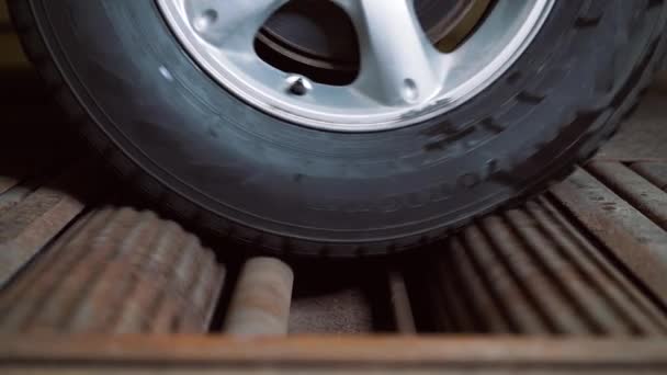Κοντά το περιστρεφόμενο τροχό του αυτοκινήτου στο περίπτερο για διαγνωστικά και τη δύναμη μέτρησης του αυτοκινήτου. — Αρχείο Βίντεο