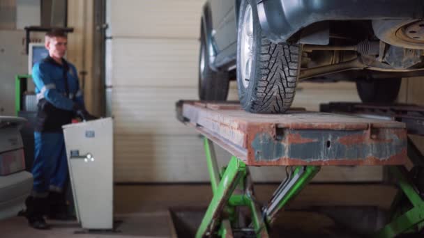 Jeune mécanicien professionnel soulève la voiture sur l'ascenseur pour effectuer le diagnostic du châssis .